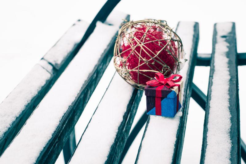 覆盖着雪花的椅子上放着一个礼物盒还有竹球