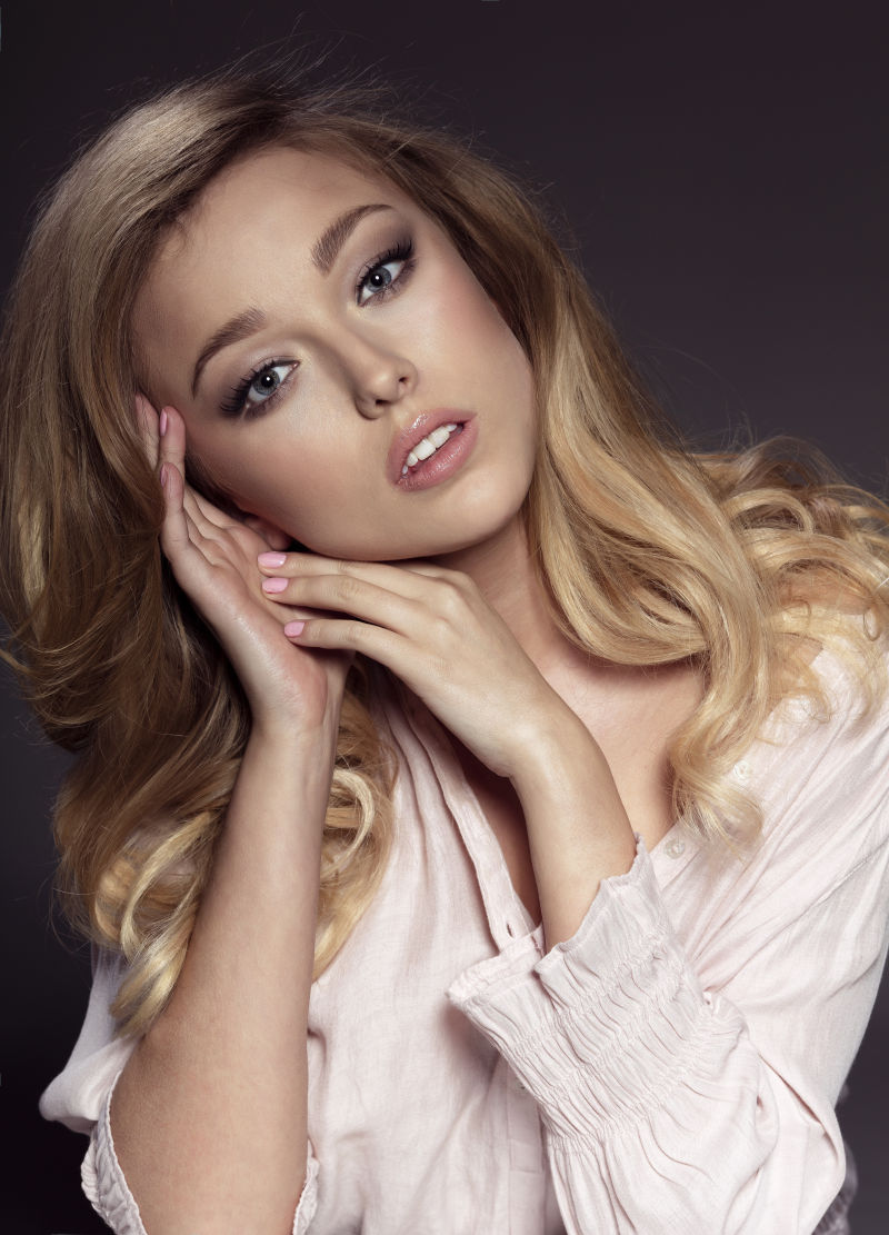 暗色背景上用手触摸脸颊的金发美女