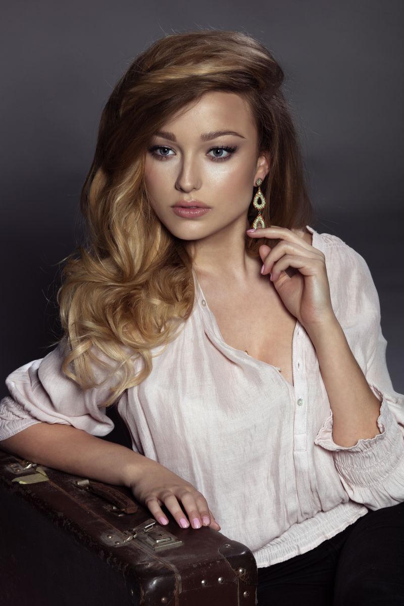 暗色背景上手放在手提箱上的金发美女