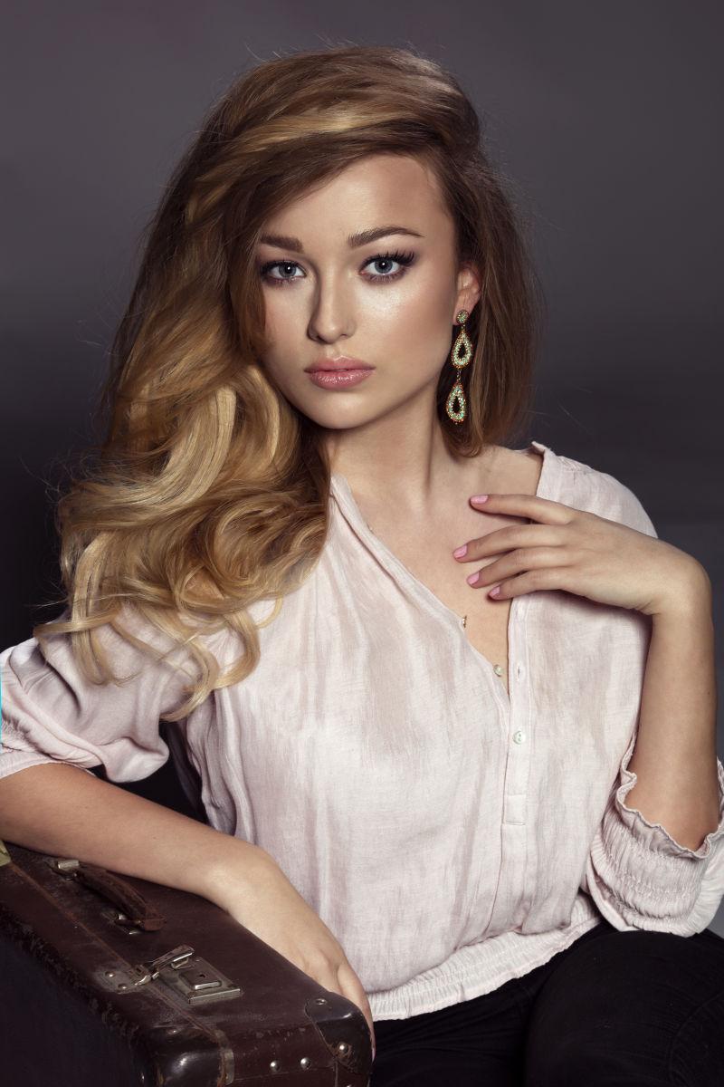 暗色背景上坐着摆姿势的金发美女