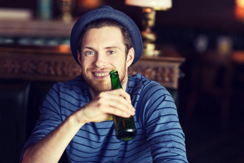 酒吧里带着蓝色帽子的男人拿着啤酒瓶