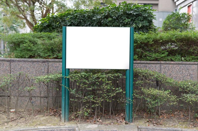 绿色植物的花坛旁的空白广告牌