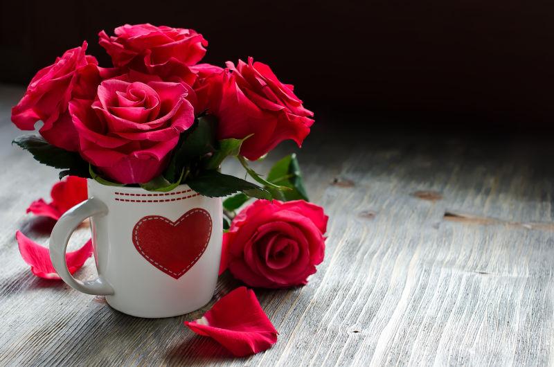 木桌上印着红色爱心的杯子里插着美丽的玫瑰花