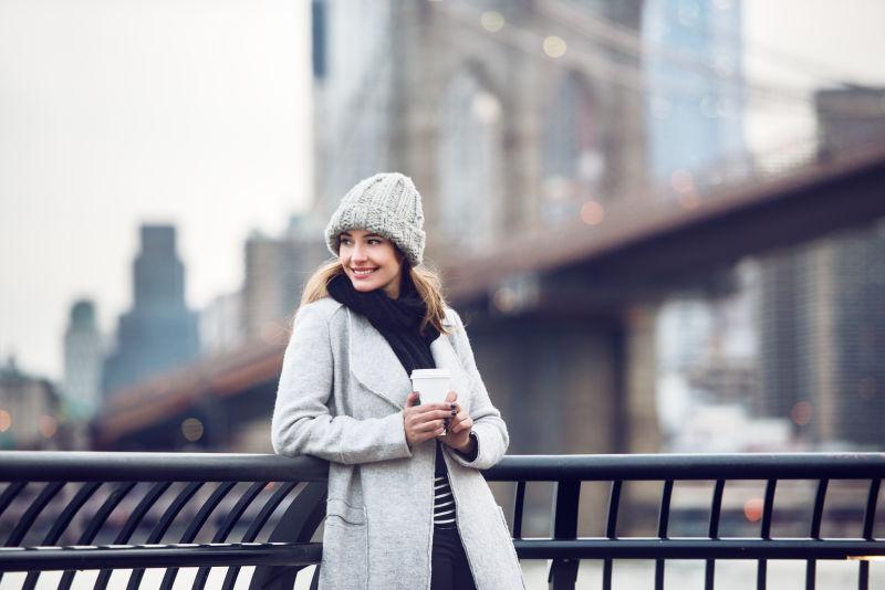 微笑的成年妇女拿着咖啡杯欣赏纽约风景和布鲁克林大桥