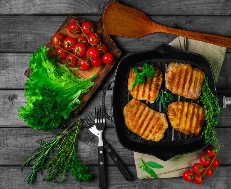 铁盘里的四份烤猪排和桌子上的蔬菜
