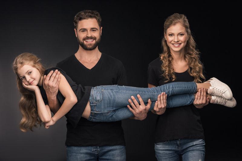 幸福的父亲和母亲抱着女儿站在黑色