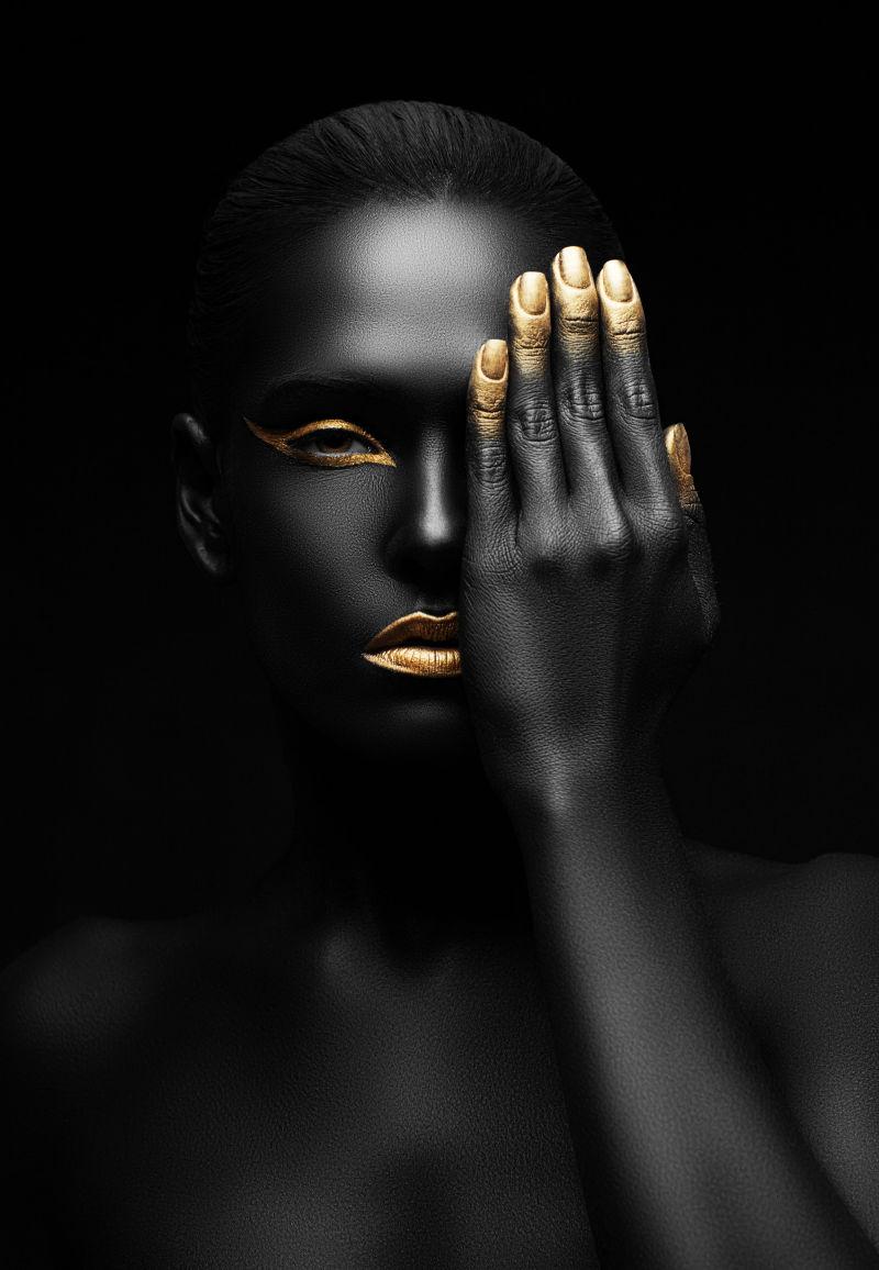 黑色背景上一个全身涂满黑色颜料的黑人用手遮住一只眼睛