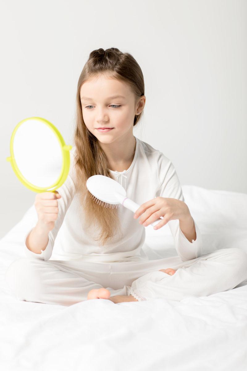 小女孩坐在床上照镜子梳头发