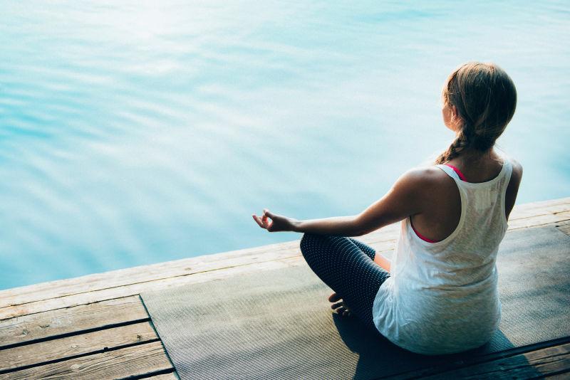 在湖边平静的水面旁练习瑜伽沉思的女人