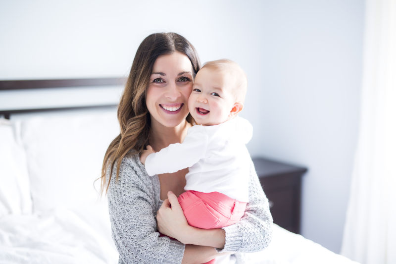 美丽母亲和可爱的婴儿躺在白色的床上