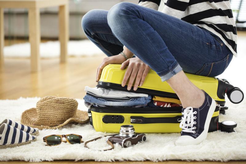 坐在旅行箱上整理衣服的女人