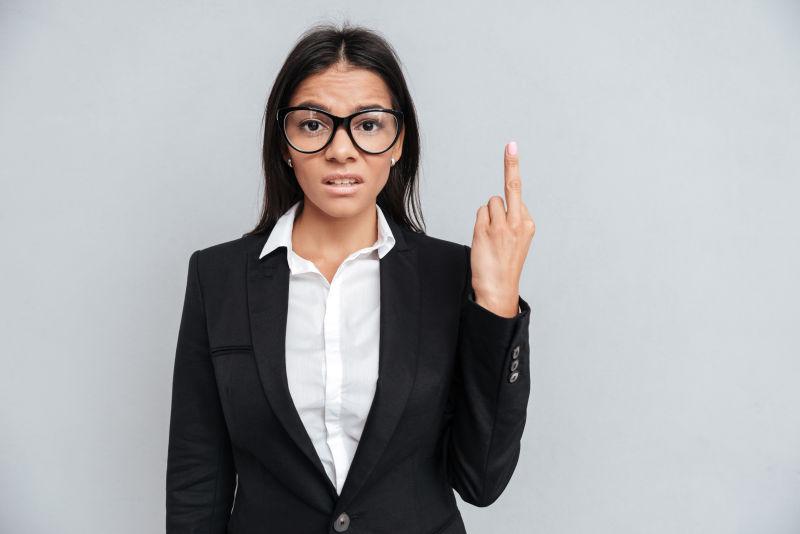 灰色背景下穿着西装的女商人在镜头中显示中指