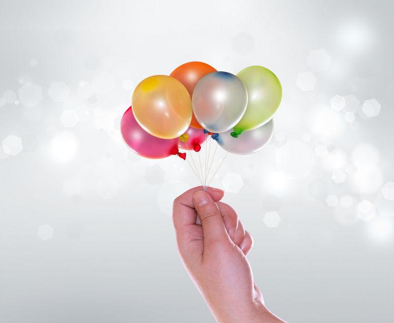 灰色背景中的带彩色气球和手