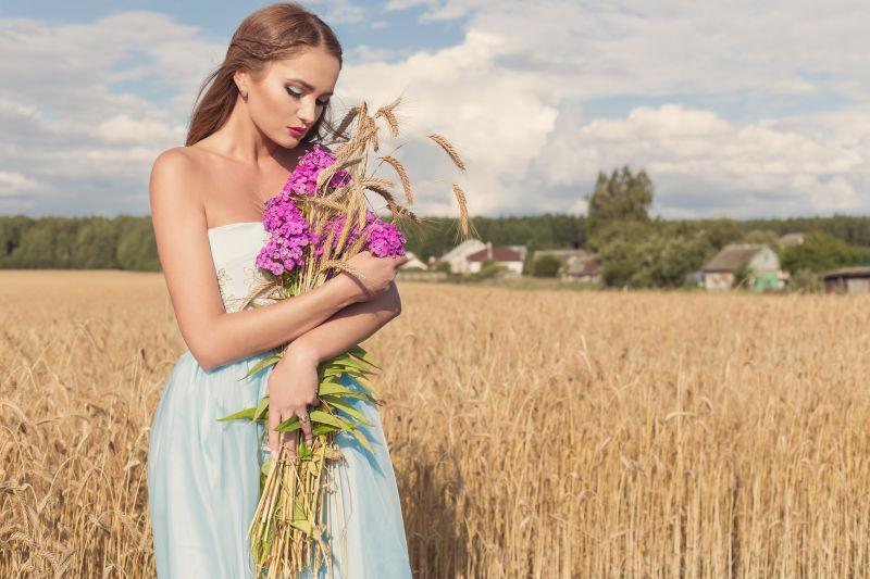 美丽的苗条女孩穿着一件蓝色的连衣裙在田野里拿着麦穗束花
