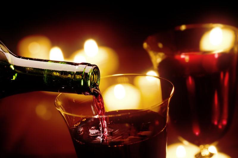 黑色有蜡烛的背景下把葡萄酒倒进玻璃杯