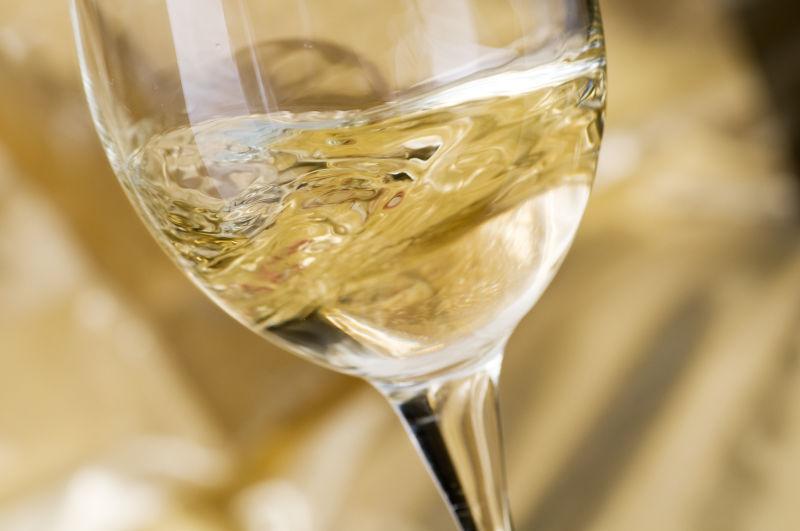 淡黄色背景下向高脚杯中倒入葡萄酒