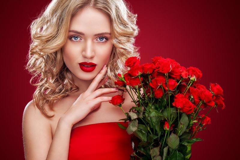红色背景中美丽的金发女人捧着一束红玫瑰