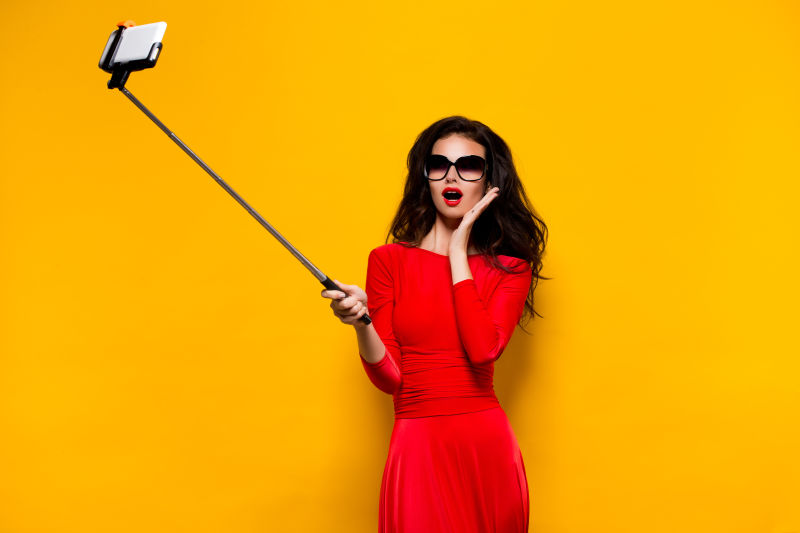 戴着太阳镜拿着自拍杆自拍的性感红衣美女