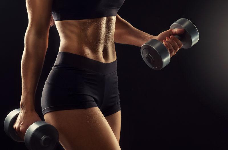 黑色背景下举哑铃的健身女人