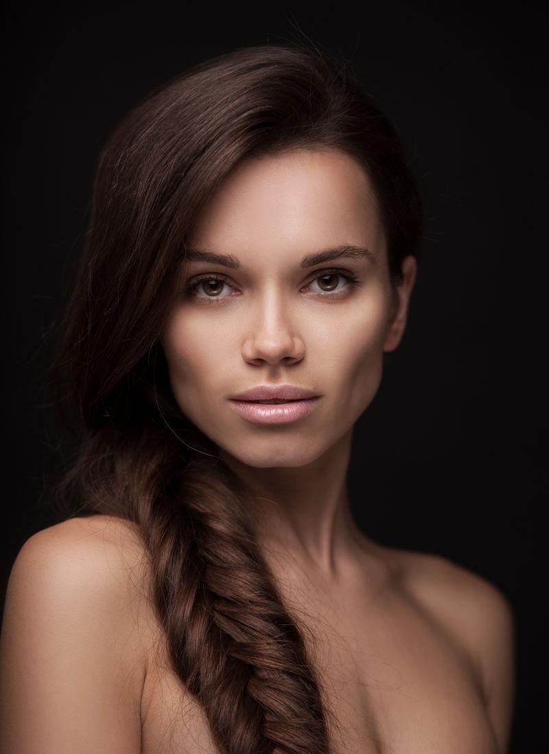 在黑色背景下的留着长长的黑色头发的美丽的年轻女人