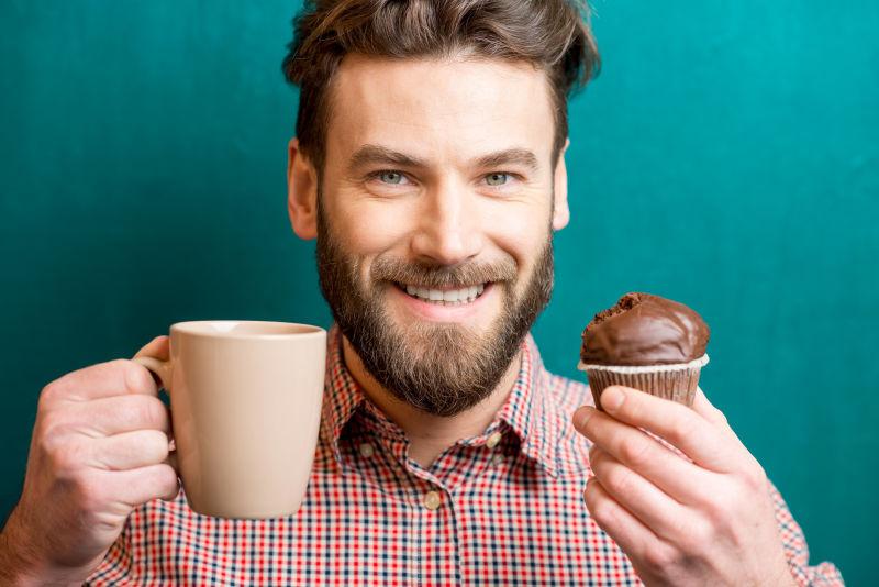 男人手里有巧克力松饼和咖啡杯