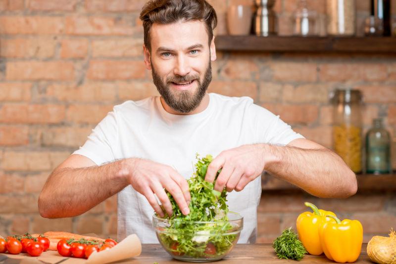 穿着白色T恤的漂亮胡子男人在厨房里做西红柿和胡椒沙拉