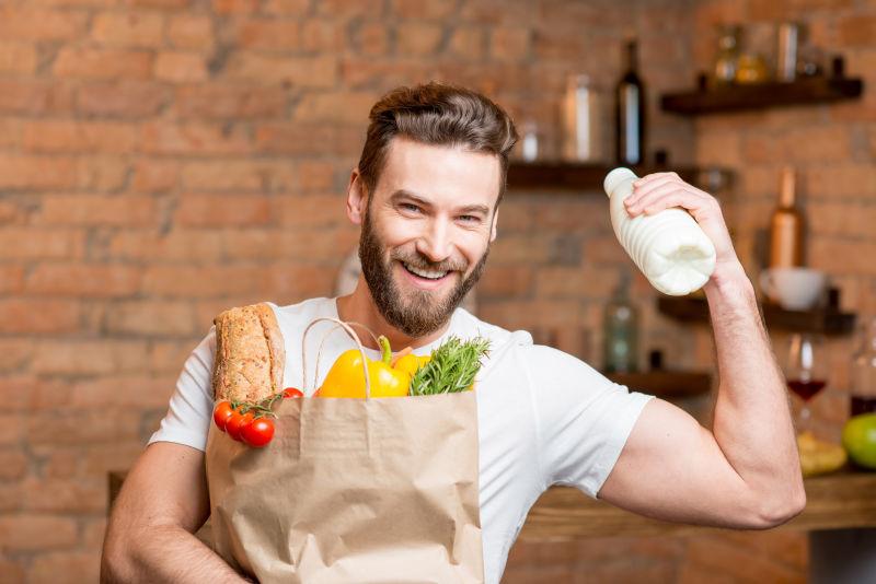 帅哥拿着袋装牛奶在厨房里摆满健康食品