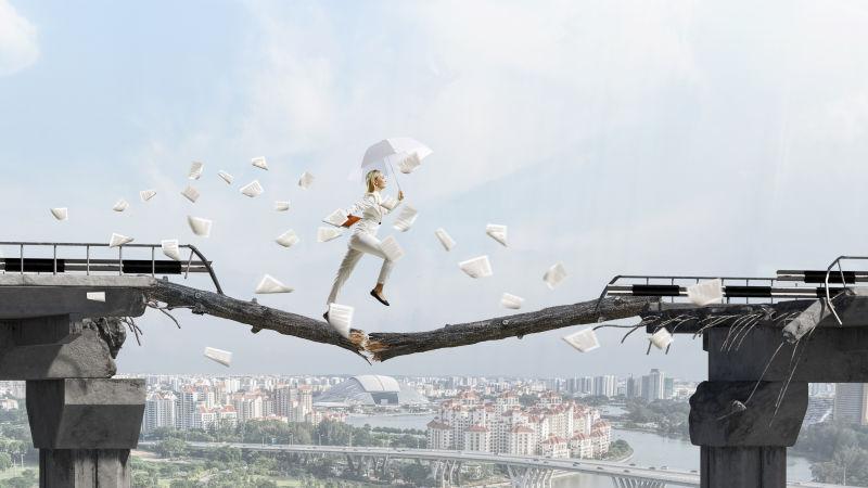 手拿雨伞的女商人在桥上断裂的独木上行走