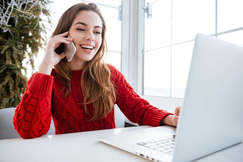 穿红毛衣的年轻美女一边用手机聊天一边用笔记本