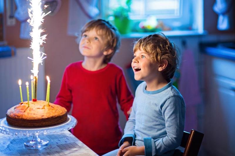 两个小男孩看着生日蛋糕上点燃的蜡烛