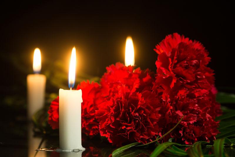 黑色背景下红色康乃馨花朵和燃烧着的白色蜡烛