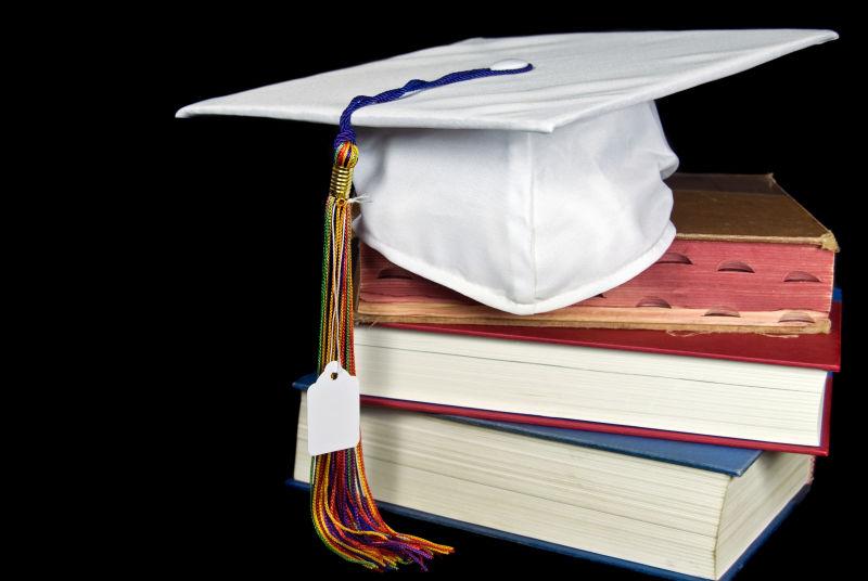 黑色背景中的书和白色毕业帽