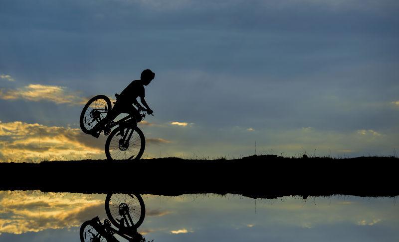 夕阳蓝天下溪边骑自行车的运动员