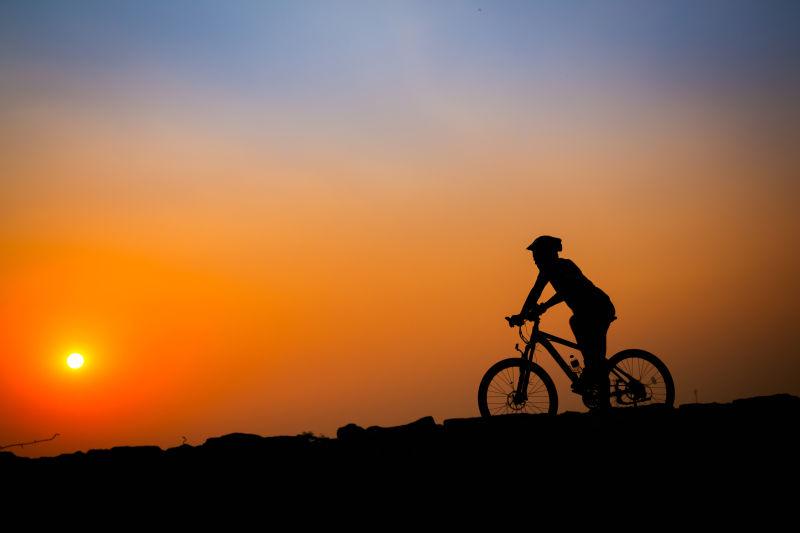 日落时年轻男子骑自行车的剪影