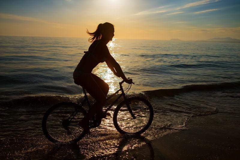 假期女人在海滩骑自行车的剪影