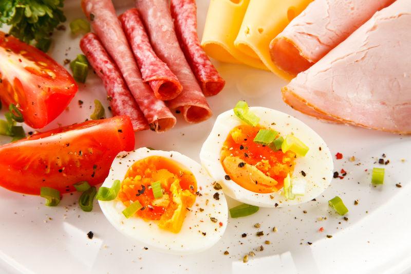 放在白色餐盘里的煮鸡蛋和火腿番茄早餐