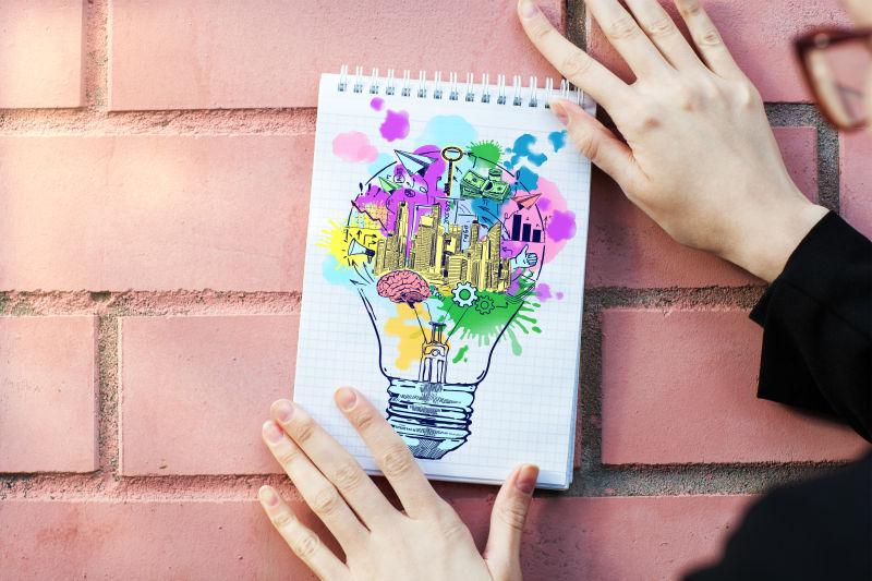 女手用红灯墙将记事本钉在有创意的灯泡上