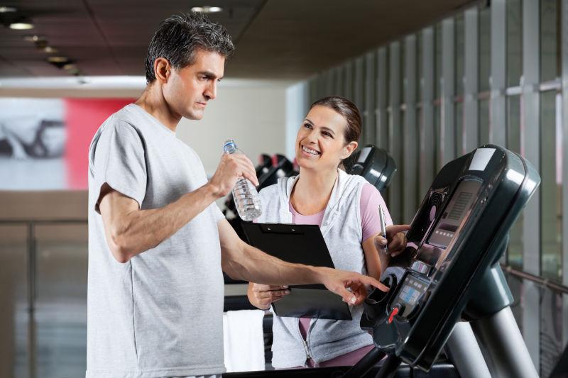 健身房跑步机上喝水的男人和女教练