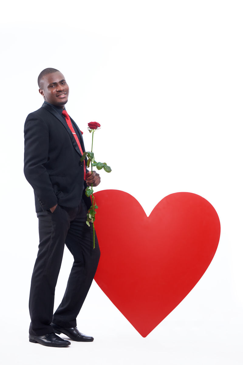 拿着玫瑰靠在红心上的黑人