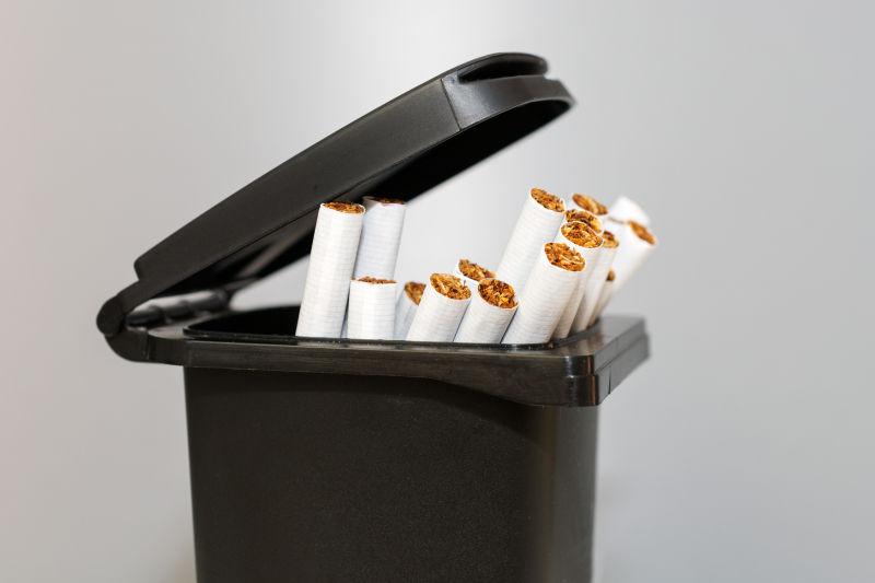 灰色背景下一堆香烟在垃圾桶里