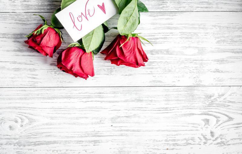 白色木桌上一束红玫瑰上的卡片