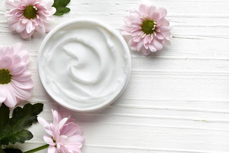 从顶上看白色奶油背景的化妆霜容器和粉红色花朵