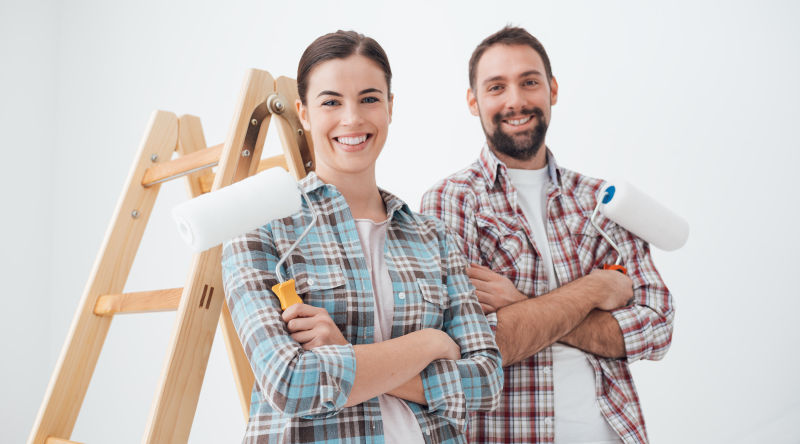 快乐的年轻夫妇微笑着拿着油漆辊