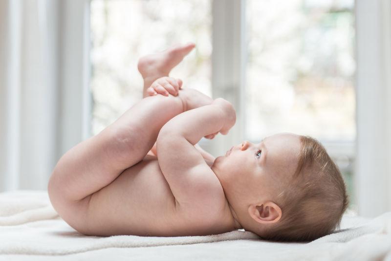 躺在床上抱着胖乎乎的小腿的可爱的小女婴