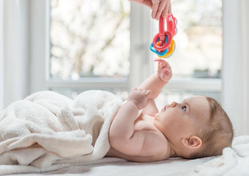 躺在床上伸手去拿玩具的小宝宝