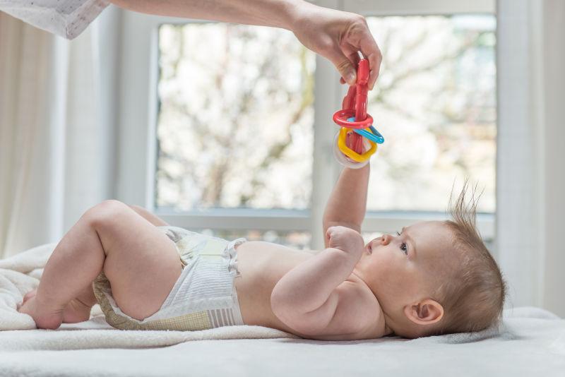 躺在床上伸手去接玩具的幸福的小婴儿