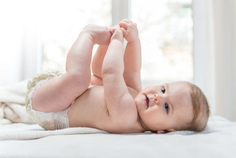 躺在床上抱着小脚丫的小女婴