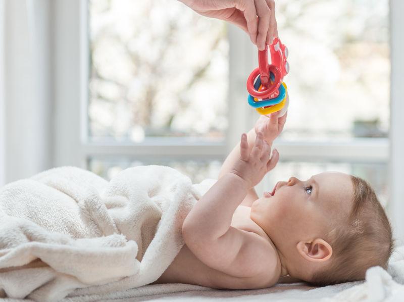 躺在床上伸手接玩具的可爱的小婴儿