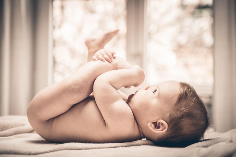 躺在床上抱着自己的腿的胖乎乎的小婴儿