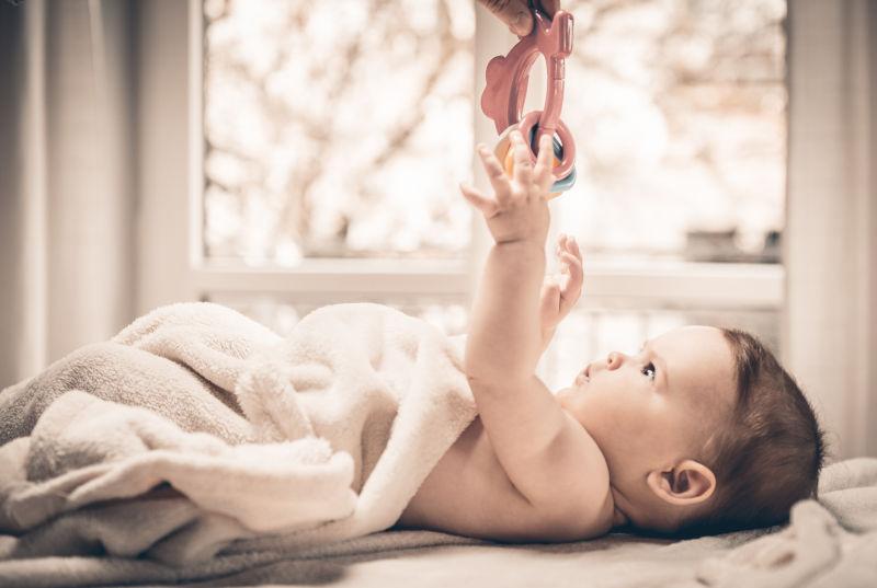 躺在床上的小婴儿伸手去接玩具